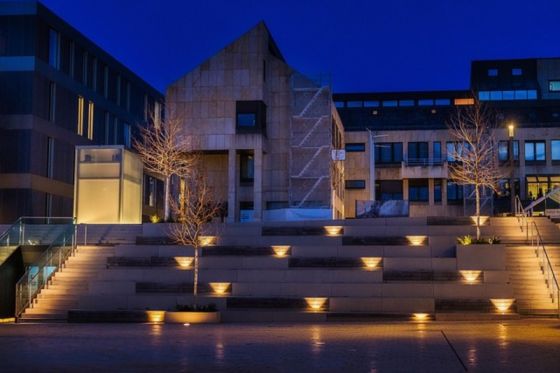 Stimmungsvoll beleuchteter Vorplatz mit breiten Treppenstufen und warmem Bodenlight vor modernem Gebäude bei Nacht
