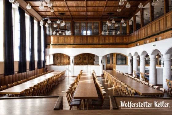 Historischer Festsaal mit langen gestellten Tafeln, Holzempore, Rundbogenarkaden und Glühbirnenleuchtern